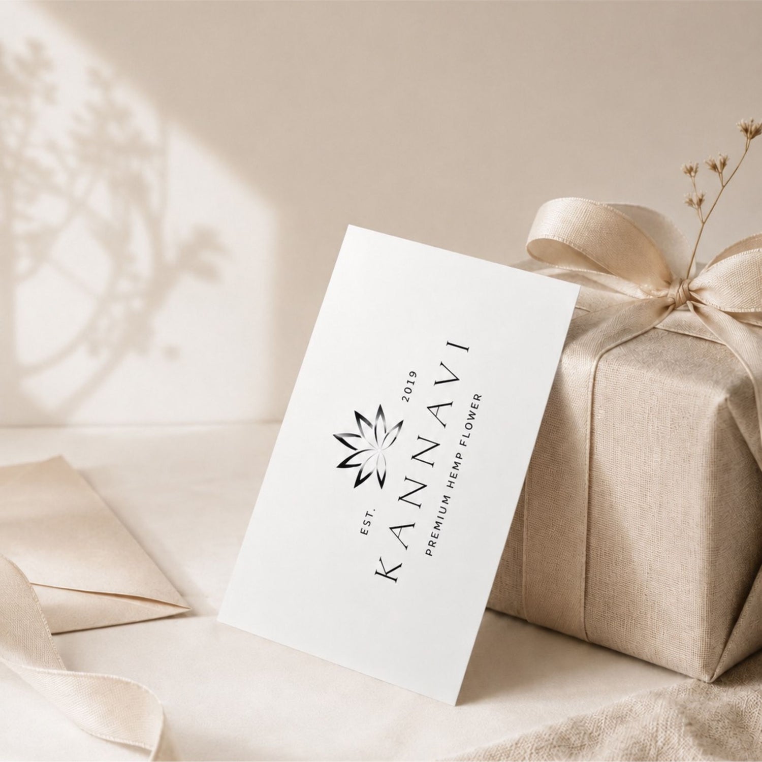 Kannavi Gutschein als stilvolle Geschenkidee mit weißer Gutscheinkarte, beige verpackter Geschenkbox, Schleife und natürlicher Dekoration.