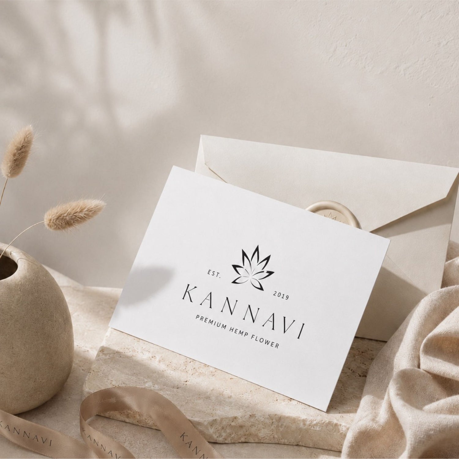Kannavi Gutschein in minimalistischer Lifestyle-Szene mit weißer Gutscheinkarte, Umschlag, Kannavi Band, Steinfläche und warmen Naturtönen.