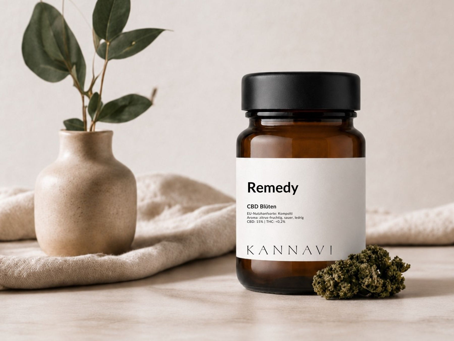 Kannavi Remedy CBD Blüten im braunen Glas mit Hanfblüte und dekorativer Vase auf hellem Stoffhintergrund