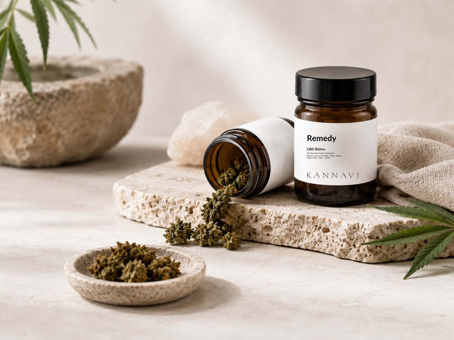 CBD Blüten mit geöffnetem braunem Glas, Hanfblüten und Hanfblatt auf heller Natursteinplatte